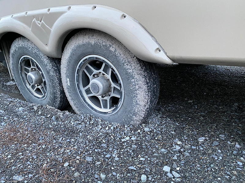 A view from the rear of the trailer showing its tires sunk into the gravelly mud at the storage yard.